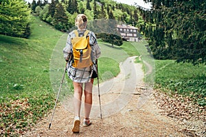 Lonely female with yellow backpack walking by mountain path with trekking poles to mount refuge hut in Slovakia, Mala Fatra region