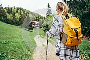 Lonely female with yellow backpack walking by mountain path with trekking poles to mount refuge hut in Slovakia, Mala Fatra region