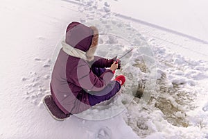 A lonely girl angler enthusiastically catches fish with a winter fishing rod sitting on a substrate