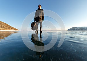 Lonely girl in black clothes with a bag standing on frozen Baikal lake on a sunny day