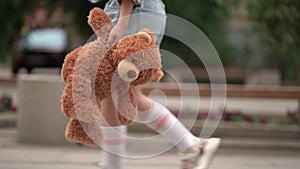 Lonely girl child with teddy bear in his hand on walk in city street