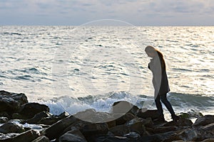 Lonely girl in a depressed mood walking along a rocky seashore