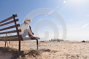 Lonely girl with glasses siting on a bench on the coast and looks sadly into the distance.