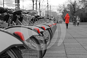 A lonely girl in a red coat takes a walk along a city street along a row of parked bicycles