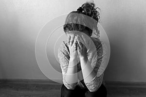 Lonely girl is sitting on the floor and crying covering her face with her hands, black and white photo