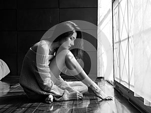 Lonely girl sitting sadly by the window in the bedroom