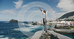 Lonely girl spreads her arms looks at the Atlantic Ocean. Woman with long blond braid hair stands with her back to