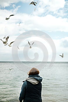 A lonely girl in a tank top and a pink sweater with a hood feeds seagulls by the sea