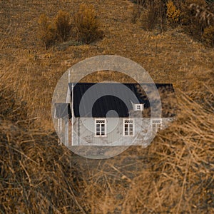 Lonely gray house with a black roof on an autumn background with yellow-orange grass.
