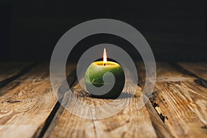 Lonely green ball-shaped candle burns on a rustic wooden table close-up