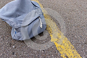 Lonely grey casual style backpack standing on asphalt road with yellow line road marking with copy space