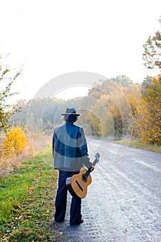 Lonely guitarist looking at empty country road in