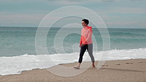 Lonely happy woman is walking on empty sandy beach against stormy sea with big waves, enjoying freedom and vacation, breathing fre