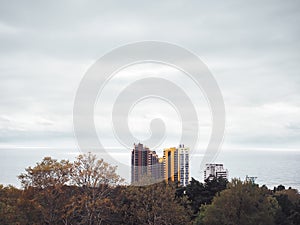 Lonely highrise buildings among autumn trees against the background of the sea and cloudy sky