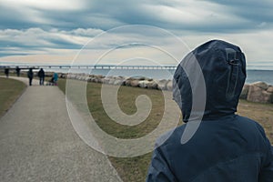 Lonely hooded female person from behind standing at seashore