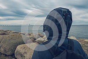 Lonely hooded female person from behind standing at seashore