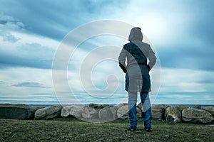 Lonely hooded female person from behind standing at seashore