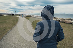 Lonely hooded female person from behind standing at seashore