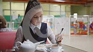 Lonely hungry schoolgirl eats in the school cafeteria during break.