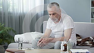 Lonely ill senior man sitting on couch and thinking about life, depression