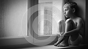 Lonely little boy looks at raindrops through the window glass