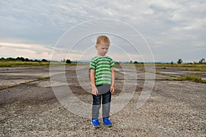 Lonely little boy stands in the field on the landing strip