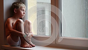 Lonely little boy waits for his parents to come home sitting on the windowsill