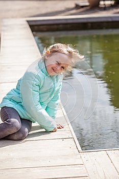 Lonely little caucasian girl sitting by lake water and looking at the camera