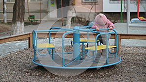 Lonely little kid girl spinning on a carousel at children's playground