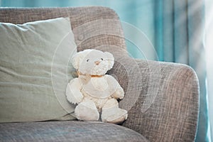 Lonely, loss and adoption with a teddy bear abandoned on a sofa in an empty living room of a home. Lost, alone and grief