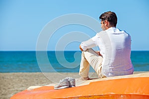 Lonely man on the beach above a boat looking at the sea