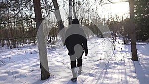 Lonely man in blue jacket and high boots walking on snowy field, sun is shining into camera, cinematic shot. Very cold