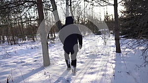 Lonely man in blue jacket and high boots walking on snowy field, sun is shining into camera, cinematic shot. Very cold