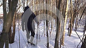 Lonely man in blue jacket and high boots walking on snowy forest with fence on the right side, cinematic shot. Very cold