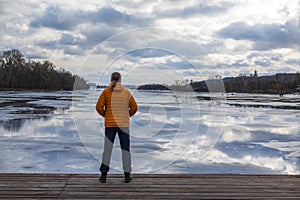 Lonely man in orange down jacket standing on a wooden pier