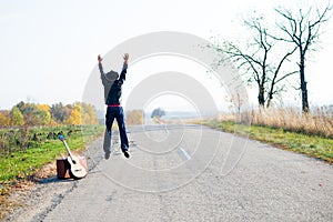 Lonely man with retro suitcase and guitar jumping