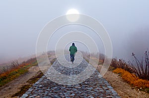 Lonely man running toward the sun on misty morning