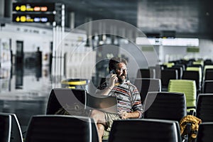 Lonely man sit down and use technology device like laptop and mobile phone at the airport gate waiting for his filght - concept of
