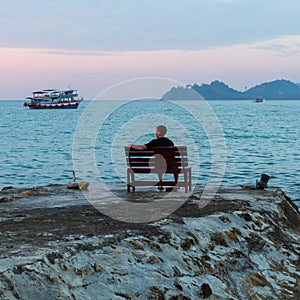Lonely man sitting on a bench looking at the sea