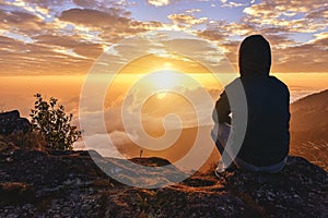 Lonely Man sitting on a mountain for watching Sunrise views alone,success and peace concept in warm