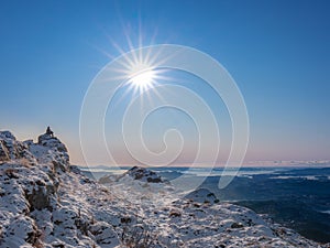 Lonely man sitting on peak of mountain in full winter sun