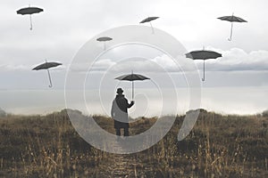Lonely man with umbrella walks down a road towards the lake and surreal black umbrellas fly in the sky