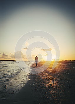 Lonely man walking on the beach at sunset