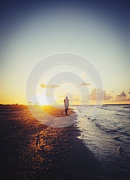 Lonely man walking on the beach at sunset