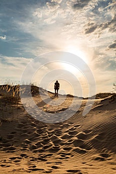 Lonely man walking in the desert dunes at sunset