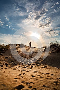 Lonely man walking in the desert dunes at sunset