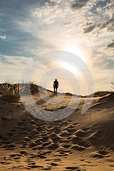 Lonely man walking in the desert dunes at sunset