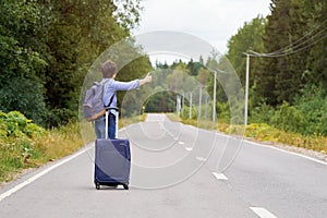 Lonely middle-aged woman with a travel bag hitchhiking on the rural road in summer