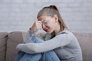 Lonely millennial woman feeling hopeless or desperate, crying on sofa at home