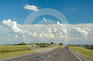 Lonely motorcyclist rides on a country road, with a sky with many clouds photo